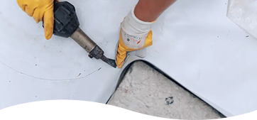 Contractor wearing yellow safety gloves applying a heavy-duty moisture barrier seal along a foundation edge.
