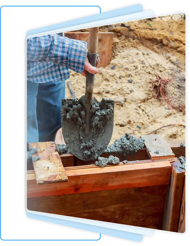 Close-up of a construction worker using a shovel to manually place wet concrete into wooden foundation forms.
