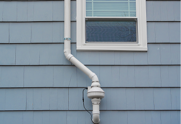 Exterior radon mitigation fan and pipe next to a window.