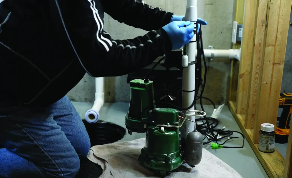Basement maintenance worker in blue uniform inspecting an active sump pump drainage system.
