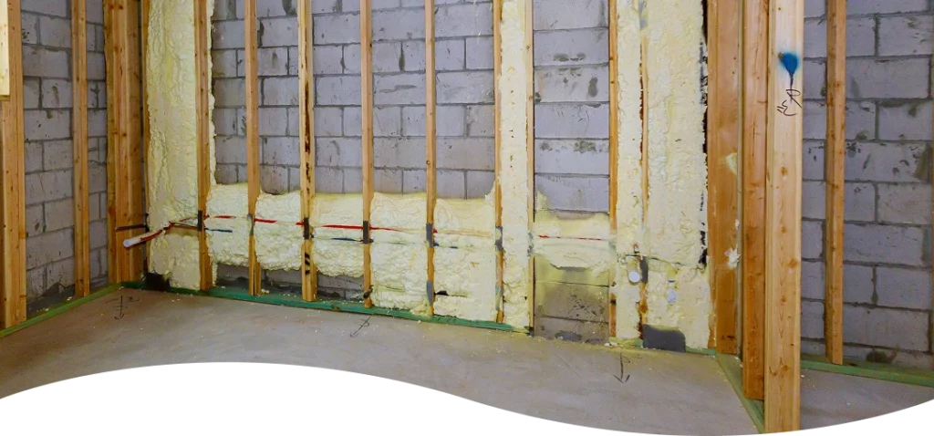 Basement block wall stabilization system showing wooden framing and yellow expanding spray foam insulation.
