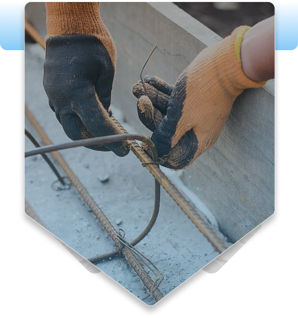 Close-up of a construction worker wearing heavy-duty gloves, tying steel rebar intersections with wire inside concrete foundation formwork.