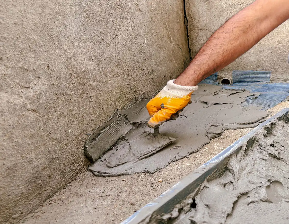 Worker using a trowel to apply fresh wet concrete for a basement floor or foundation slab repair.
