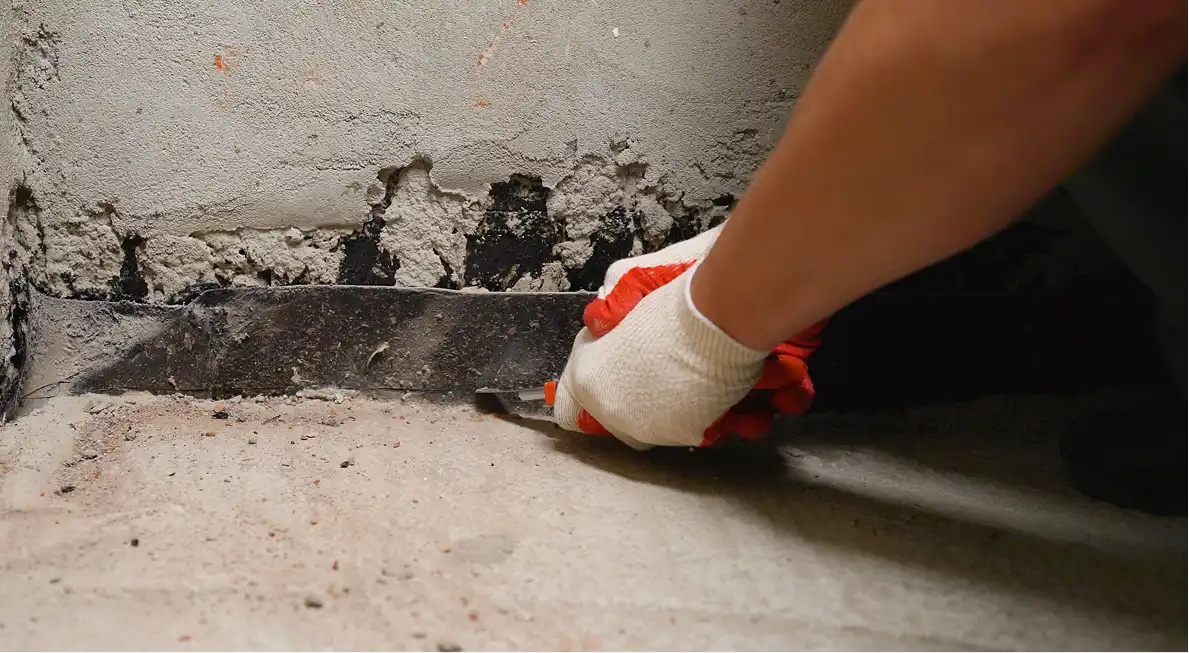 Worker scraping a concrete basement wall joint.